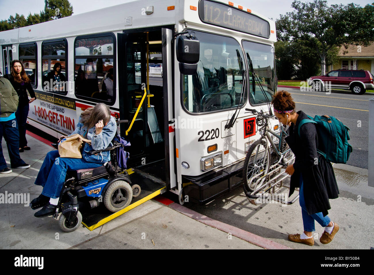 A handicapped community college student in a motorized wheelchair boards a city bus using a folding ramp in Long Beach, CA, Stock Photo