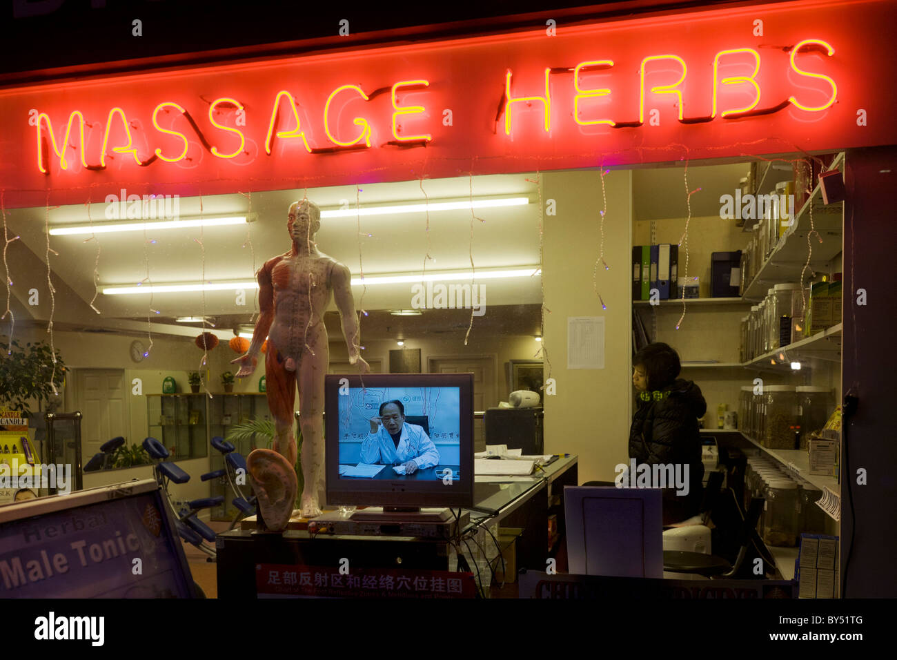 Tired assistant with Doctor on TV screen at a traditional Chinese herbalist's shop window in London's West End. Stock Photo