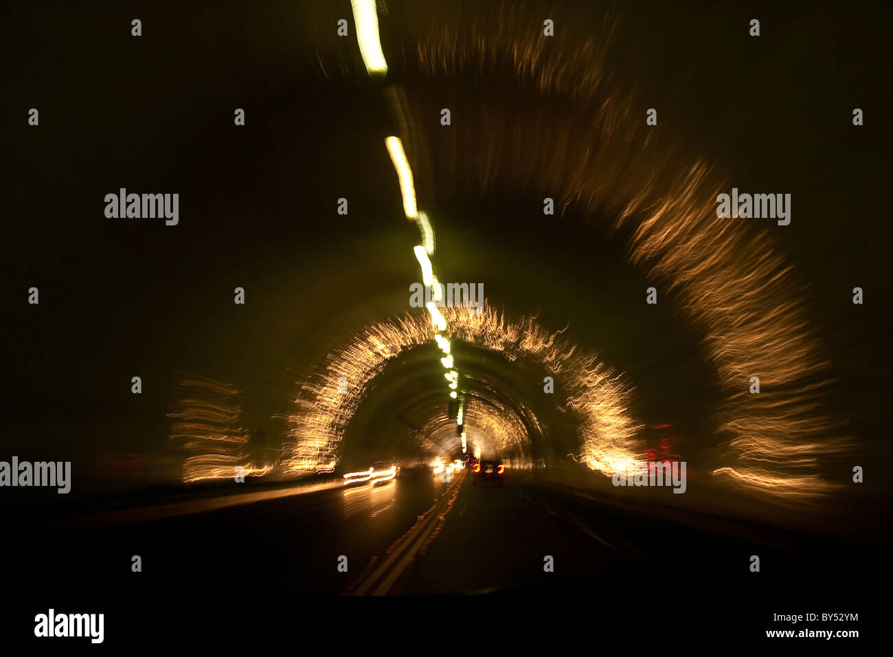 Car speeding through a tunnel with head lights and tail lights reflecting off  dome and sides of the tunnel in blur of motion Stock Photo