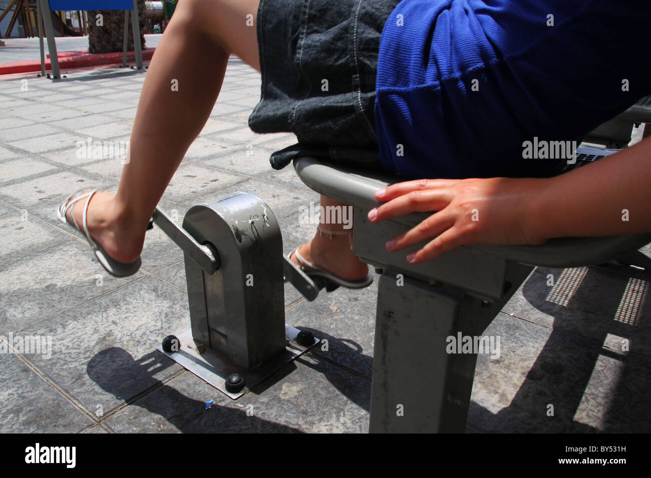 Young girl using exercise cycle in town square Stock Photo