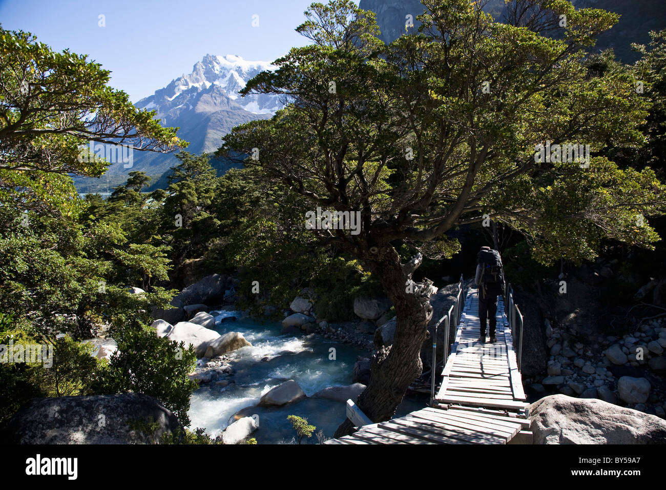 A person crossing a river while hiking through mountains, Patagonia, Chile Stock Photo