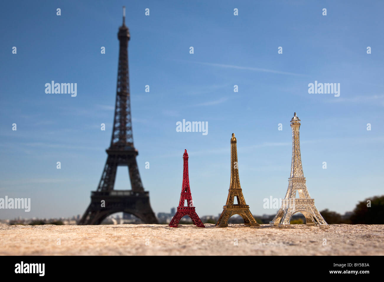 Three Eiffel Tower replica souvenirs next to the real Eiffel Tower, focus on foreground Stock Photo