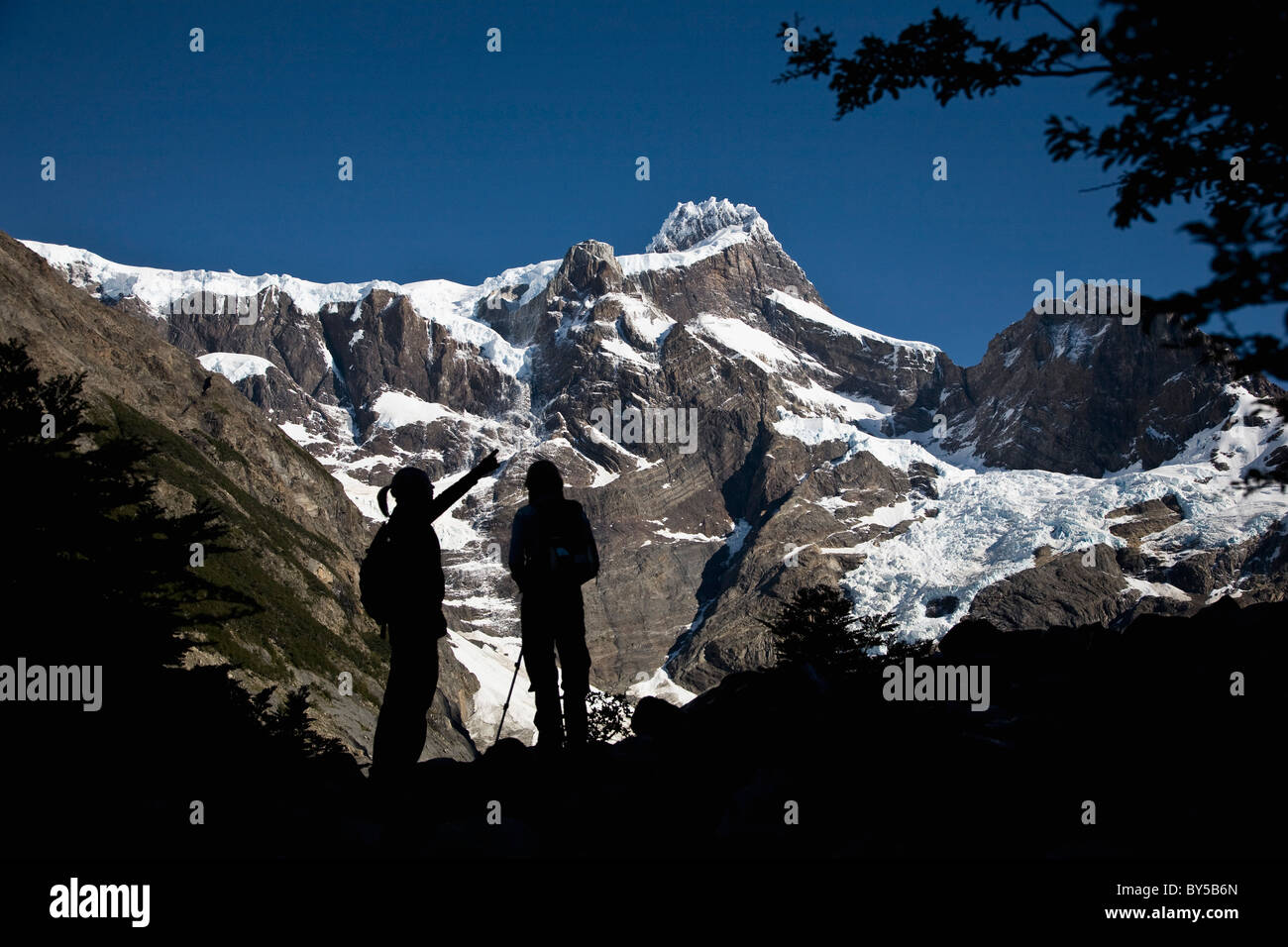Two people in silhouette standing below snowy mountains, Torres del Paine National Park, Chile Stock Photo