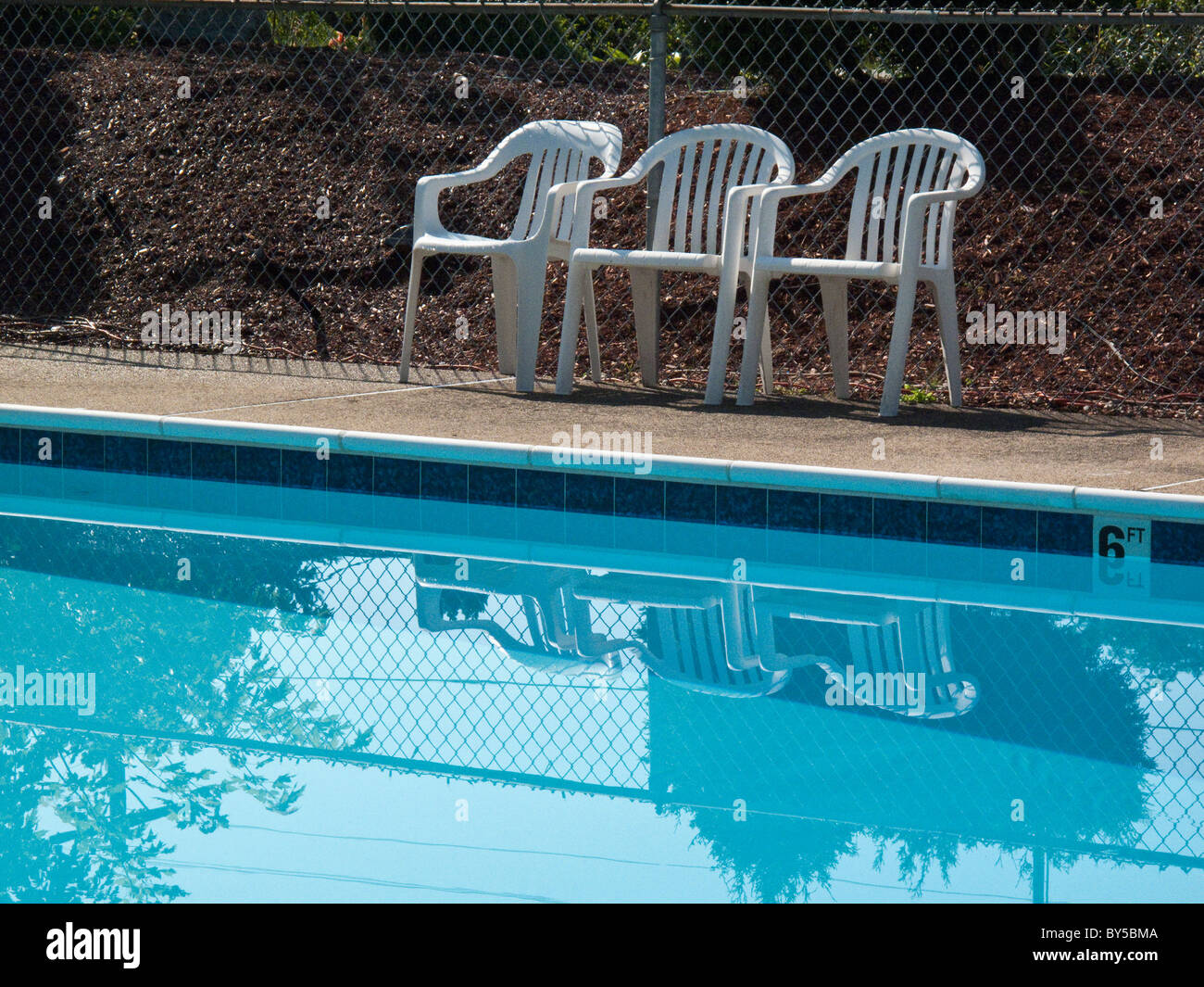 Three plastic outdoors chairs at the edge of a swimming pool Stock