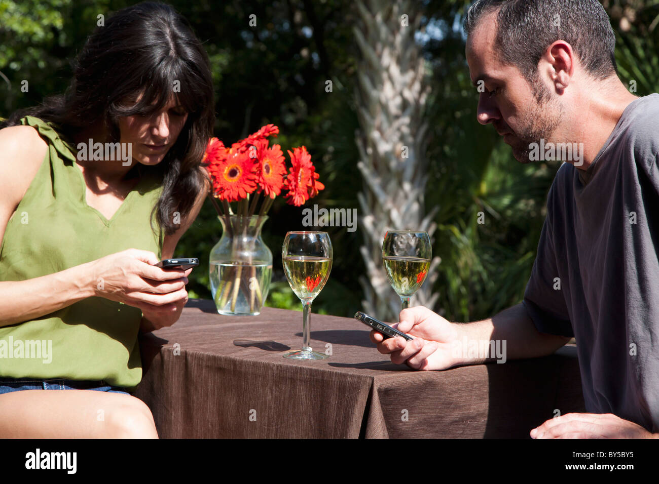 A man and woman text messaging on separate mobiles while on a backyard deck Stock Photo