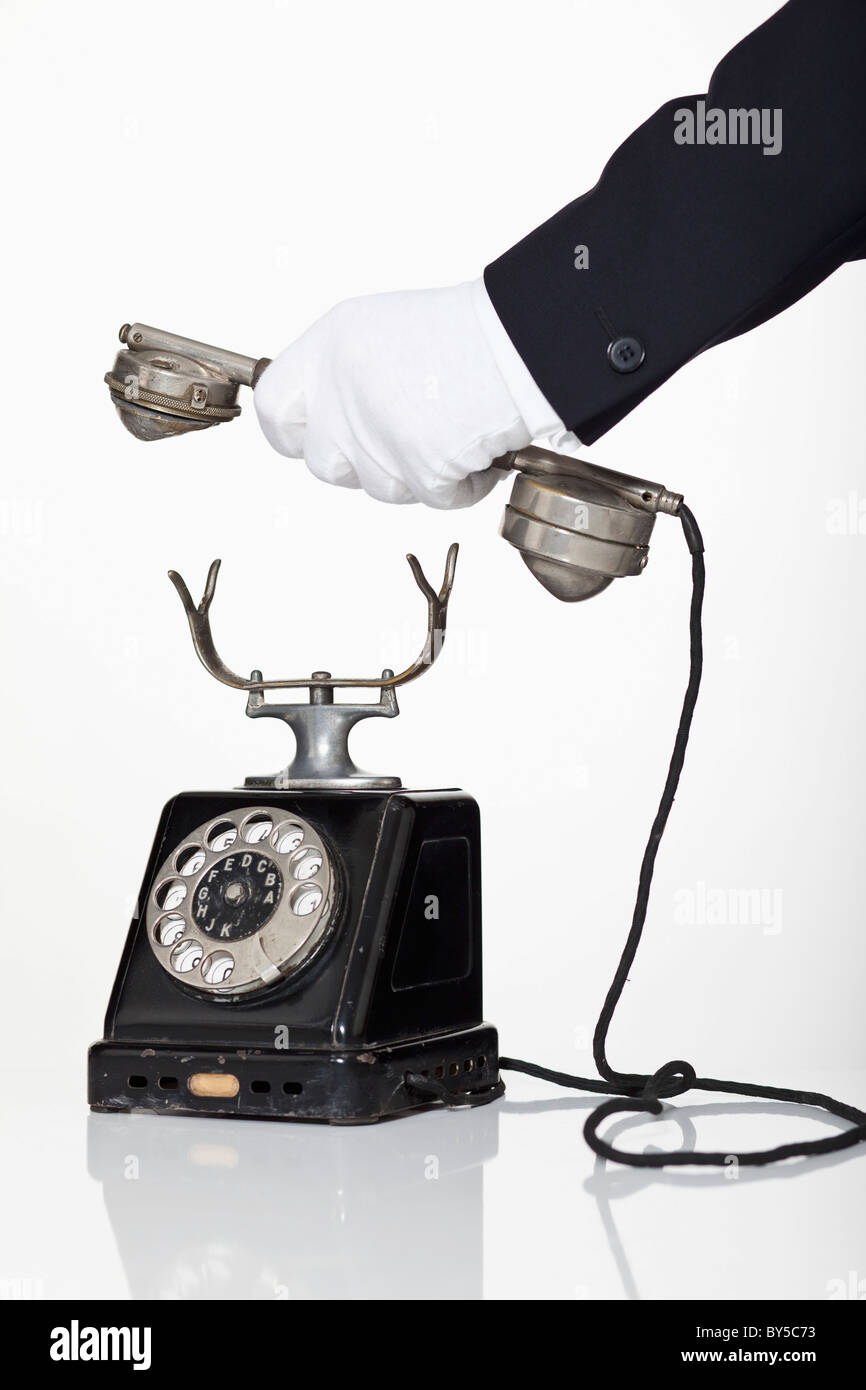 A butler holding the receiver of a rotary phone, focus on hand Stock Photo