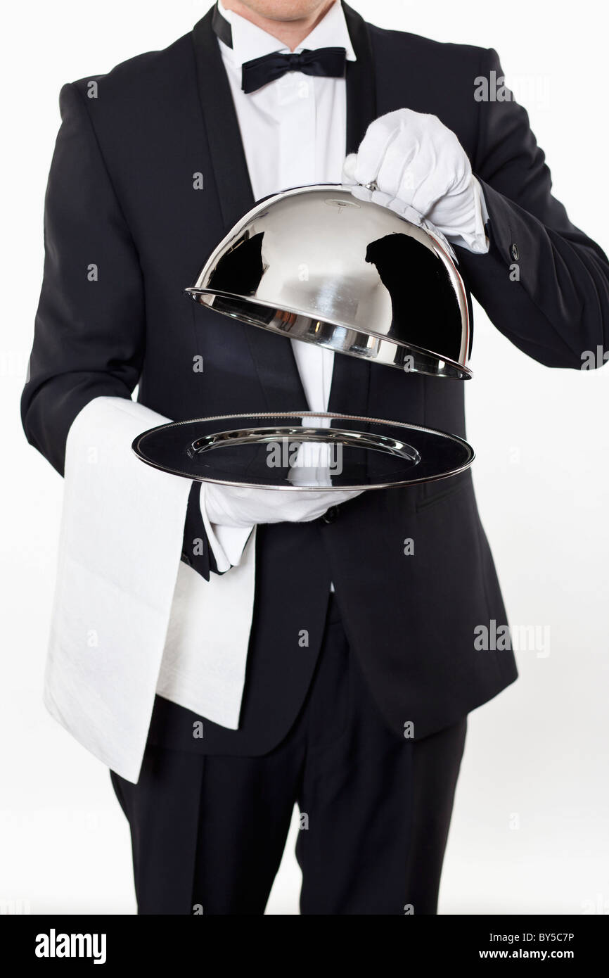 A butler taking the domed lid off an empty silver tray Stock Photo