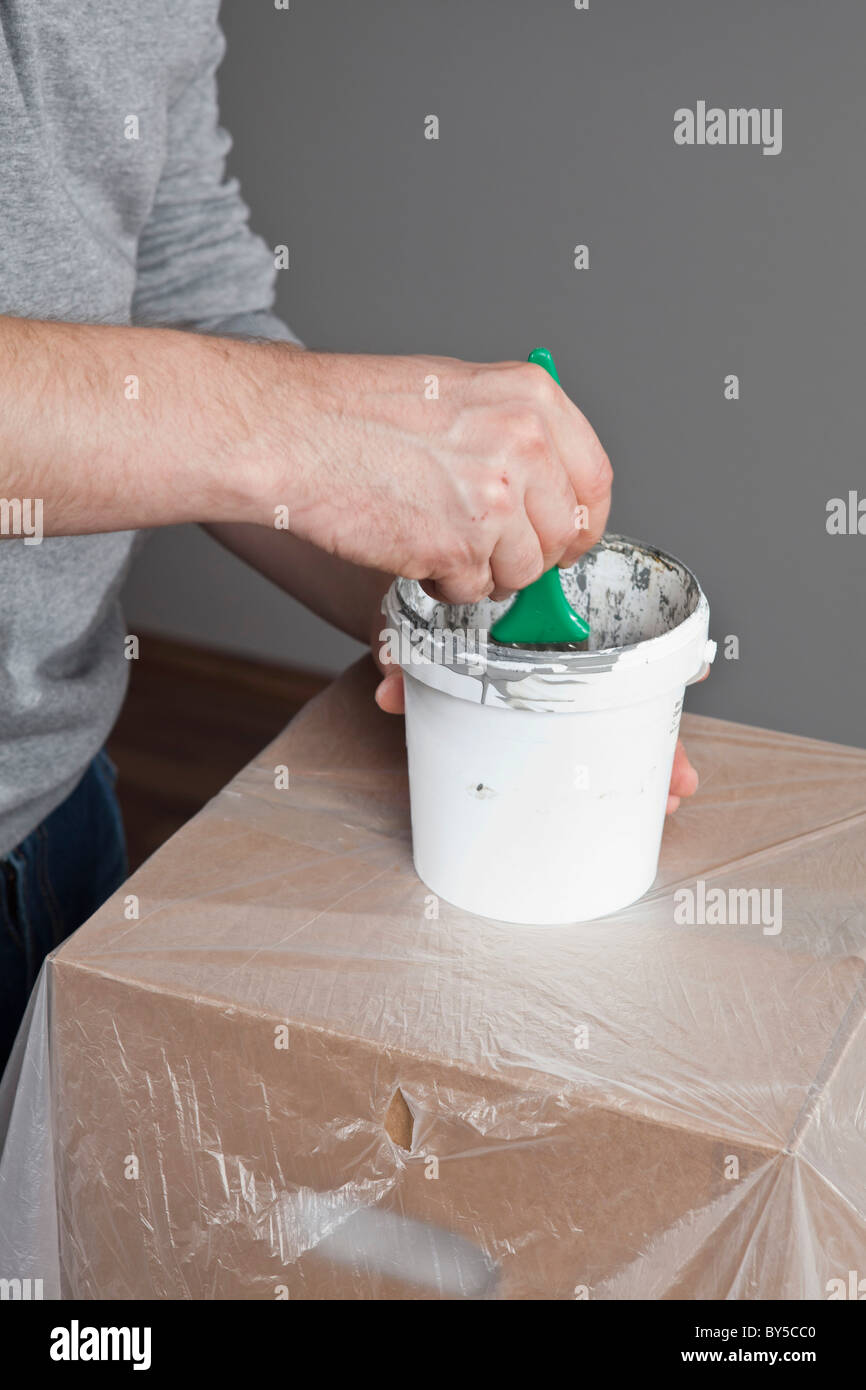 A man dipping a paintbrush into a paint can, focus on midsection, hand Stock Photo
