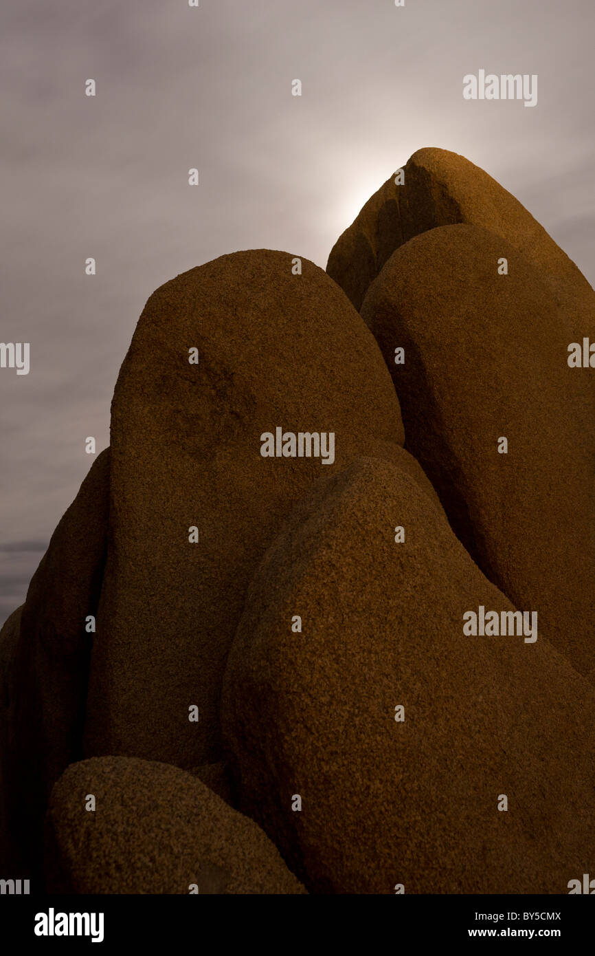 Moon shining from behind large granite boulders at night in Joshua Tree National Park, Mojave Desert, California, USA. Stock Photo