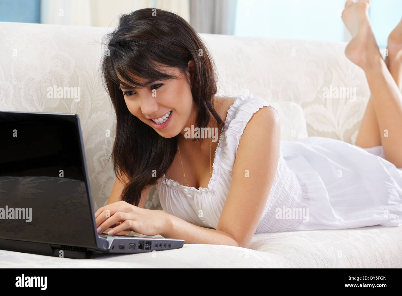 Young Asian female using laptop on sofa Stock Photo - Alamy