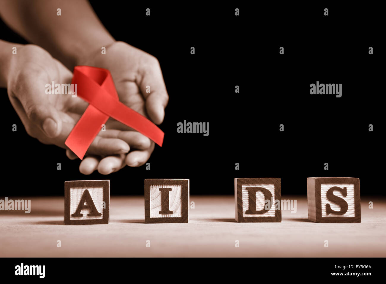 Hand holding red ribbon on back of AIDS letter blocks Stock Photo - Alamy