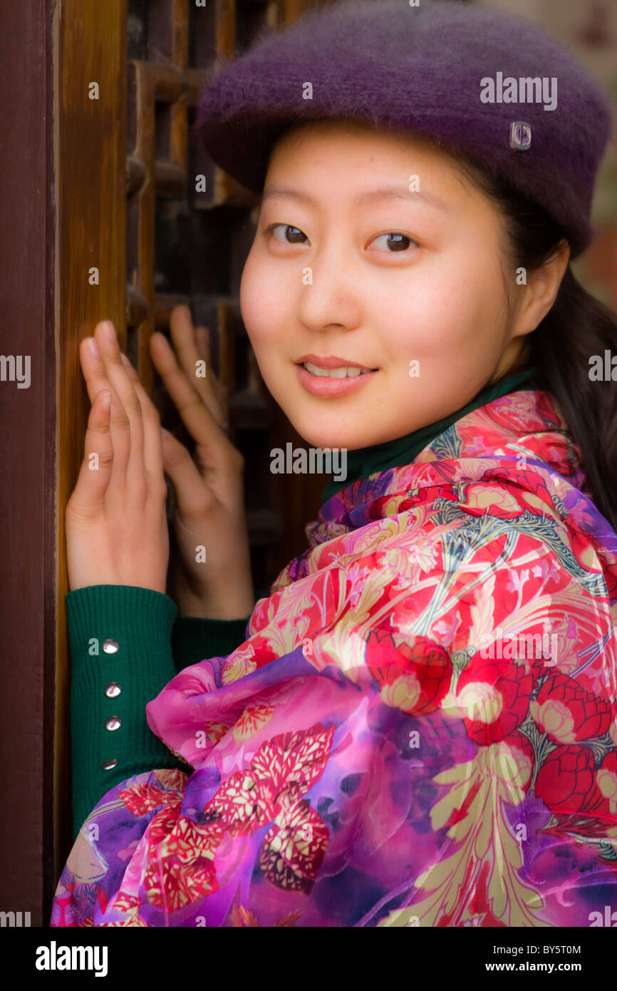 Beautiful smiling young Chinese girl wearing colourful floral silk pashmina and purple cap in Huanglongxi, China. JMH4360 Stock Photo
