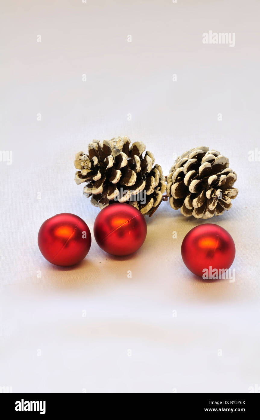 Three red Christmas baubles and two pine cones on a white background. UK December 2010 Stock Photo