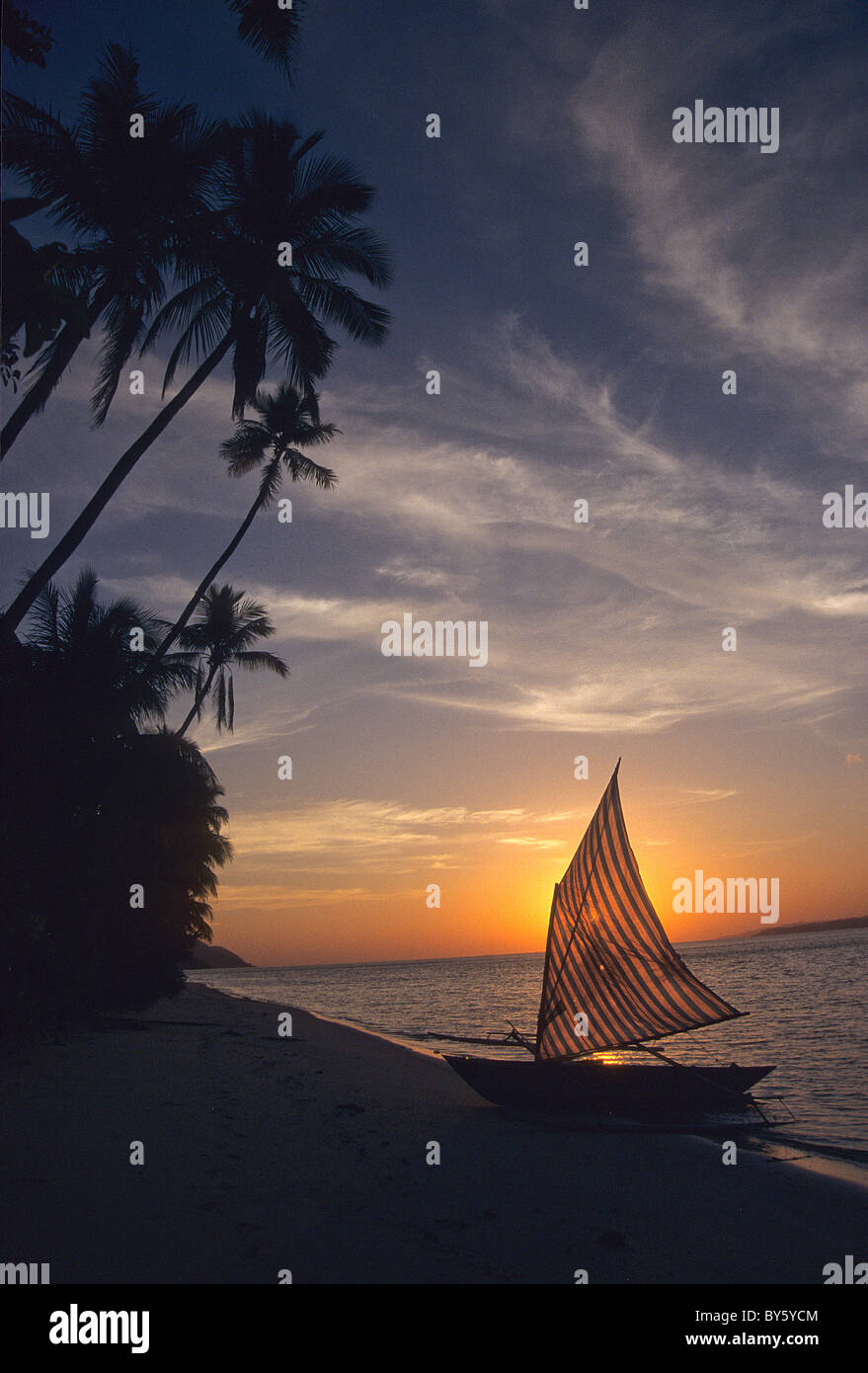 Traditional sailing canoe sitting on beach at sunset Stock Photo