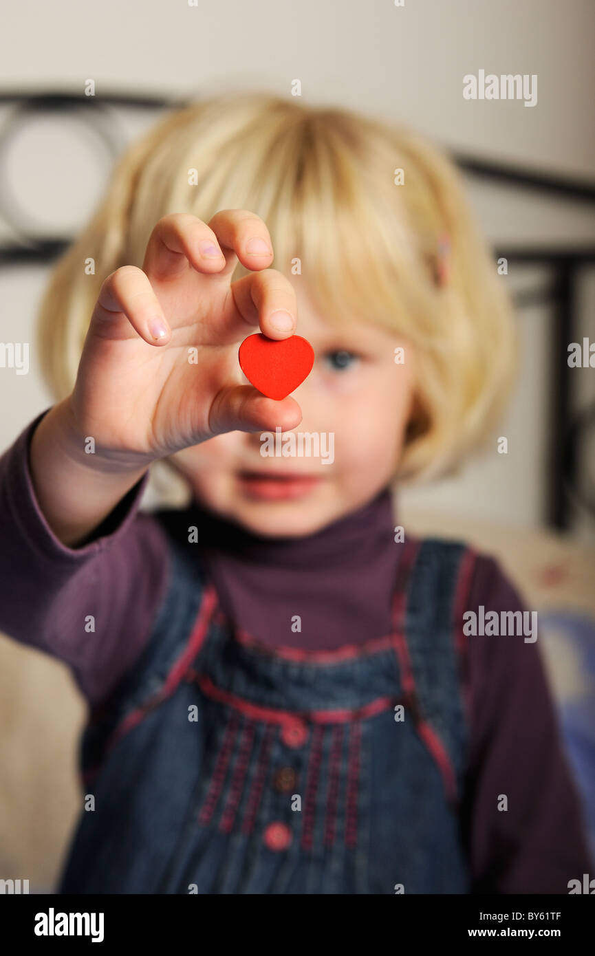 Stock photo of a five year old girl holding out a red heart shape in her hand. Stock Photo