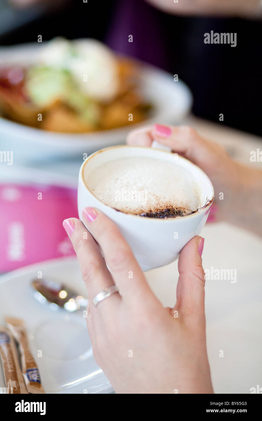 A woman's hand grips a cappuccino coffee drink at a cafe with friends. Stock Photo