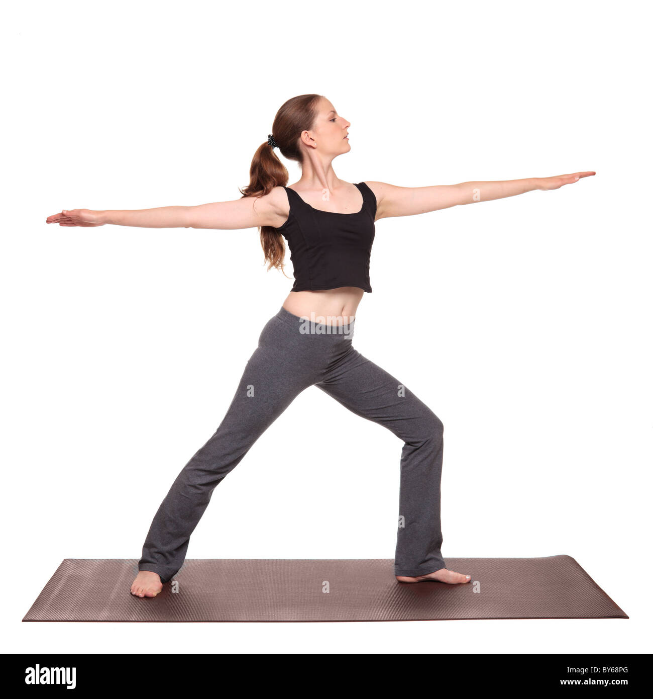 Isolated studio shot of a fit Caucasian woman holding the vrabhadrasana Warrior 2 Pose yoga position on an exercise mat. Stock Photo