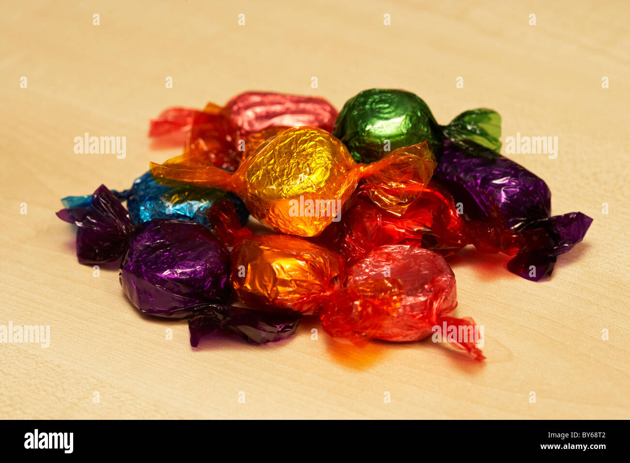 pile of wrapped up chocolate sweets in colourful wrappers on a wooden surface Stock Photo