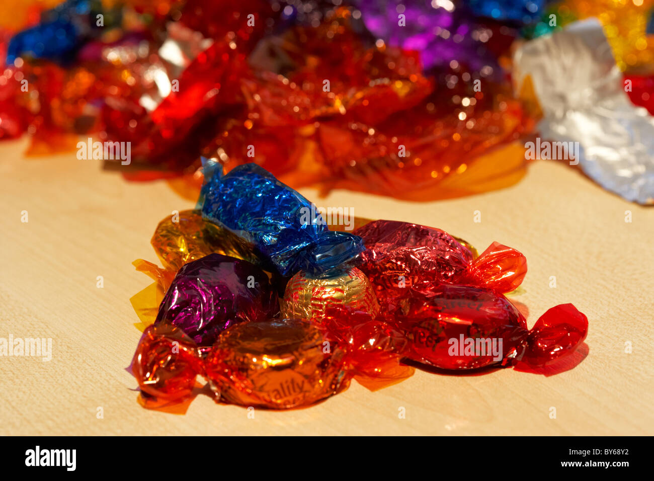 pile wrapped up quality street chocolate sweets with pile of empty colourful wrappers in the background Stock Photo