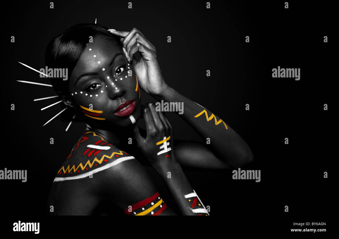 Beautiful exotic African female fashion face with tribal yellow red and white makeup cosmetics and sticks in hair. Stock Photo