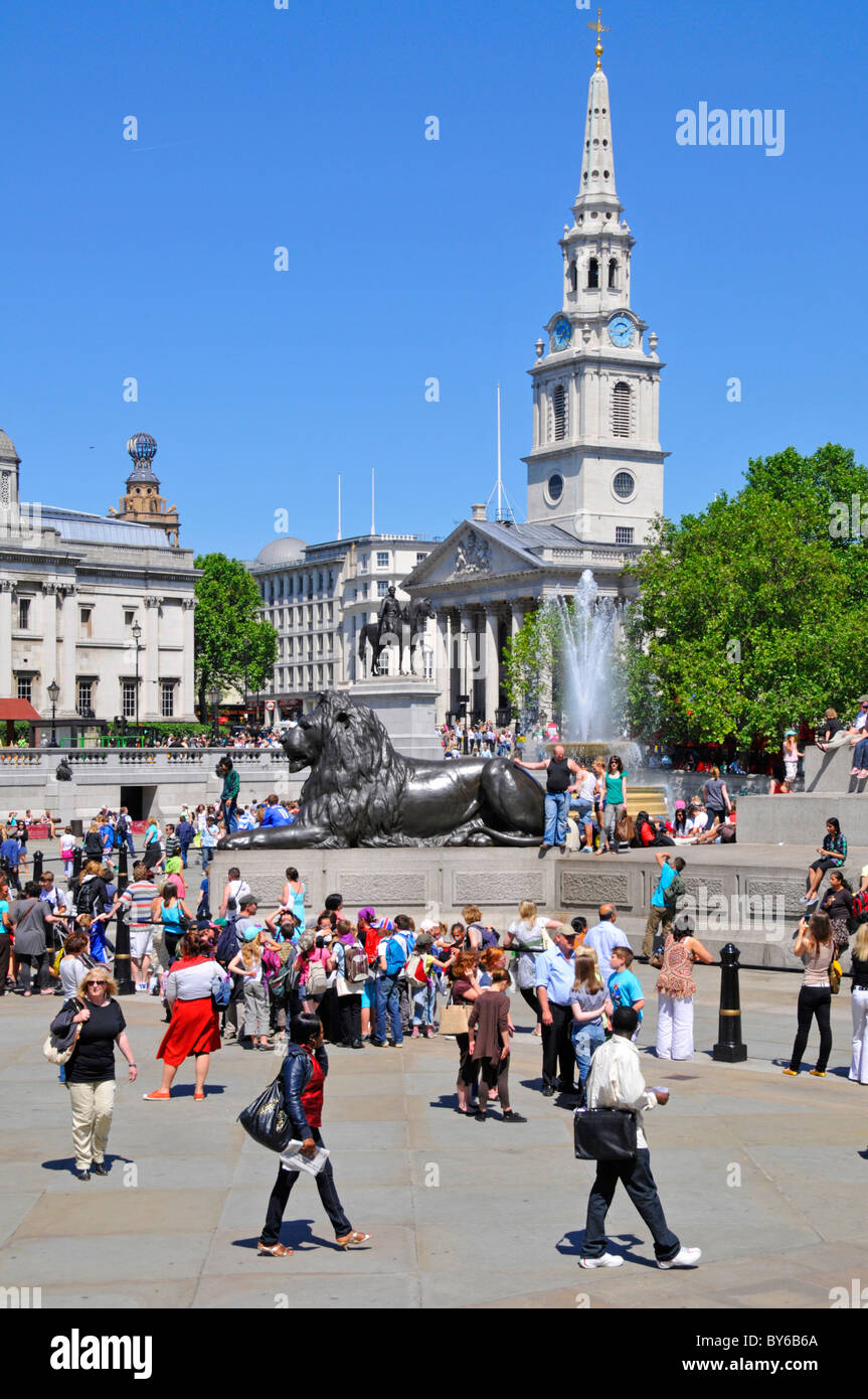 Tourists in Trafalgar Square London England UK iconic view of tourist attraction with Lion sculpture & St Martin in the Fields church & spire beyond Stock Photo