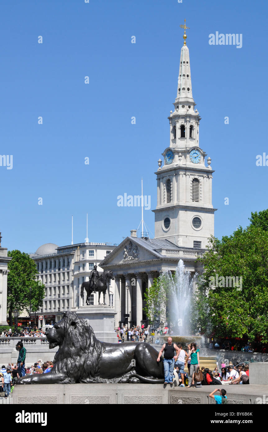 Tourists beside fountain water feature and monumental bronze lion in Trafalgar Square with Anglican St Martin-in-the-Fields church & spire London UK Stock Photo