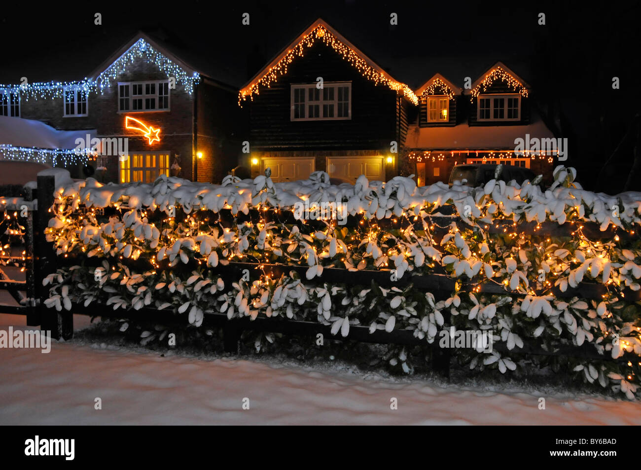 Snow covered front garden laurel hedge winter scene white Christmas lights decorations and illuminations on house gable end beyond Essex England UK Stock Photo