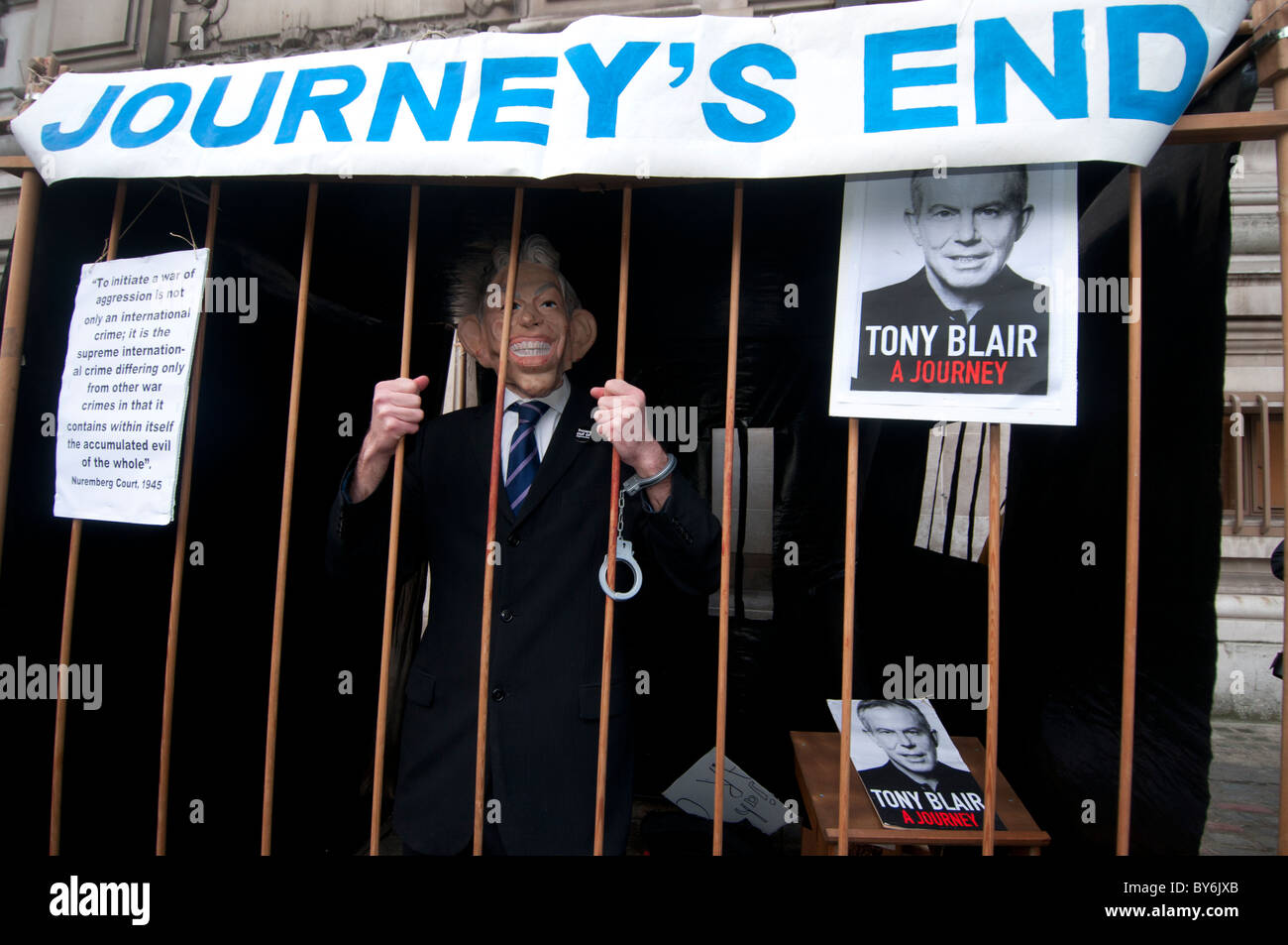 A protester dressed in a suit and a Tony Blair mask is handcuffed to a cage with the lettering Journey's End above Stock Photo