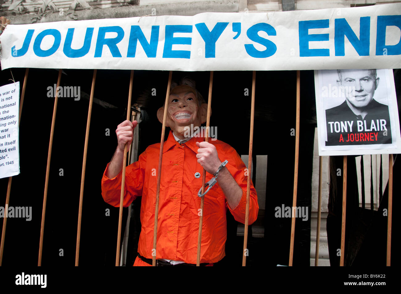 A protester dressed in an orange jumpsuit and a Tony Blair mask is handcuffed to a cage with the lettering Journey's End above Stock Photo