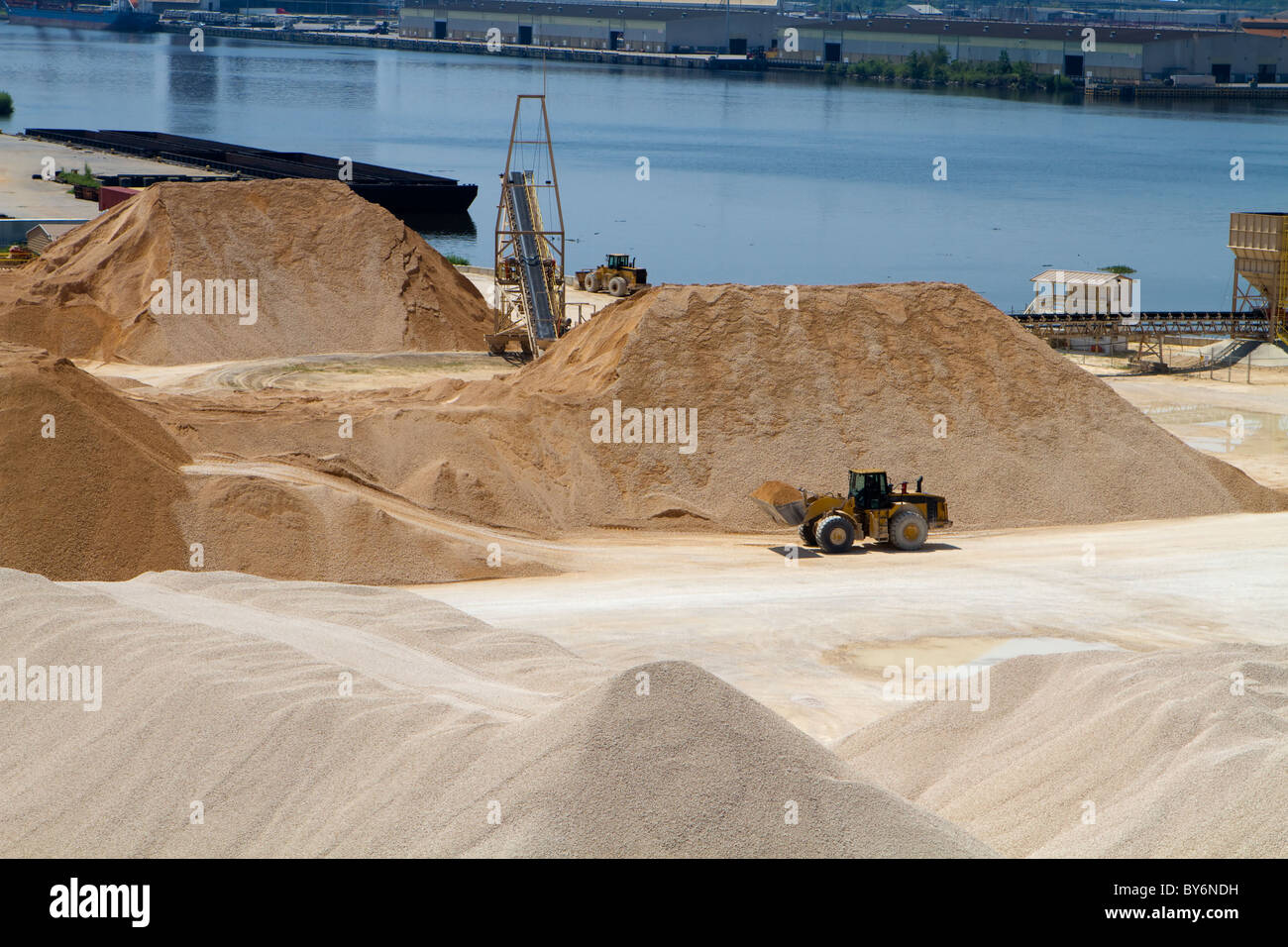 Front end loader moves gravel at a gravel and materials storage operation plant by a river. Stock Photo