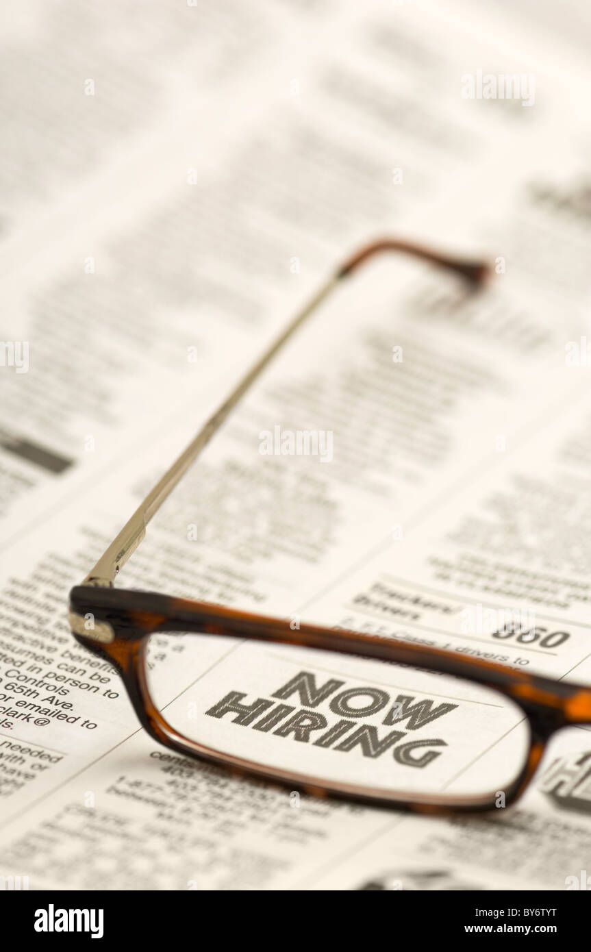 A pair of reading glasses laying across a newspaper, with the words NOW
