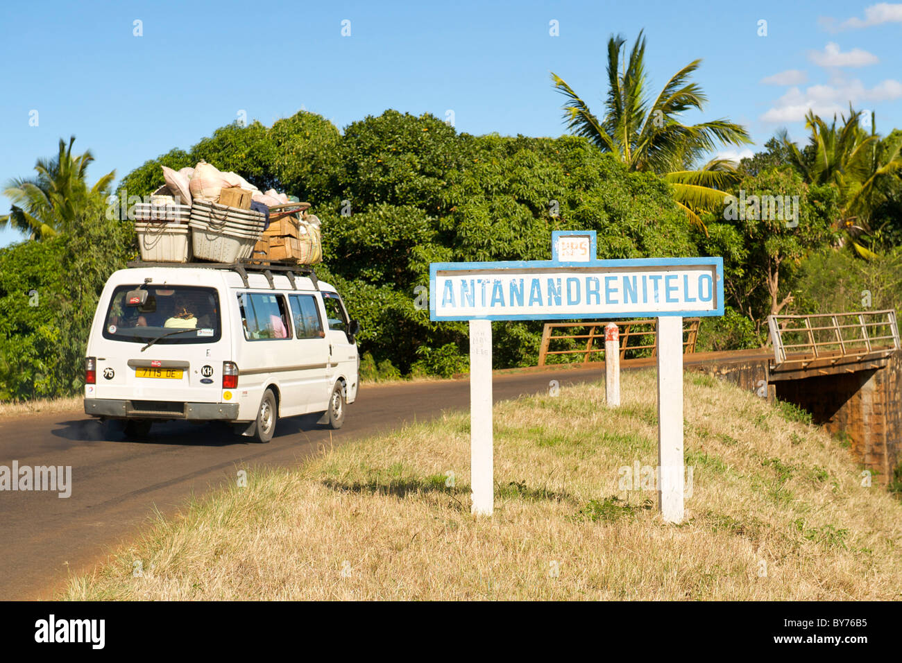 Taxi brousse (bush taxi) driving past a road sign for the village of
