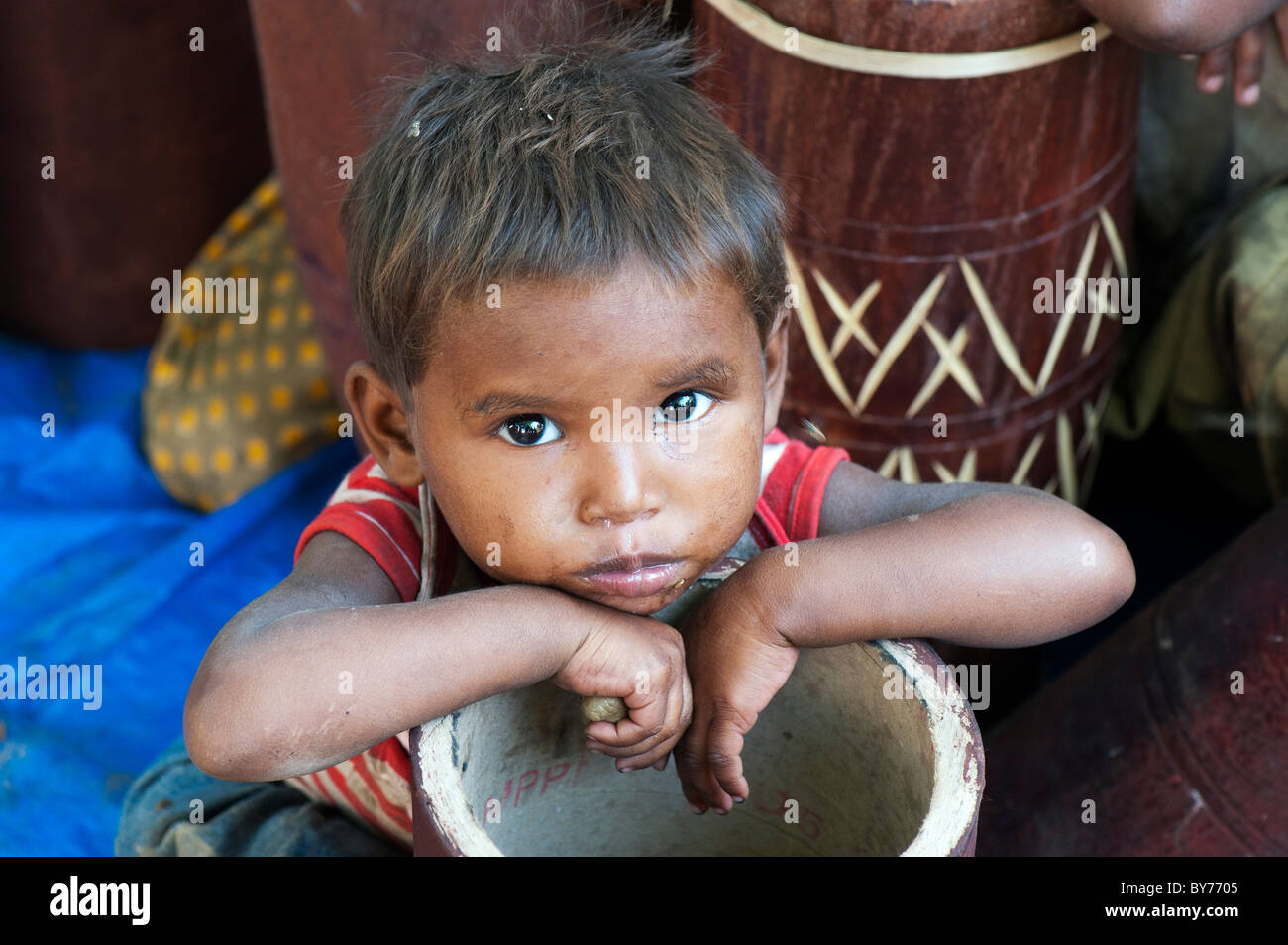 Young poor lower caste Indian street baby boy from Utter Pradesh leaning on half made drums. The drum makers children. Stock Photo