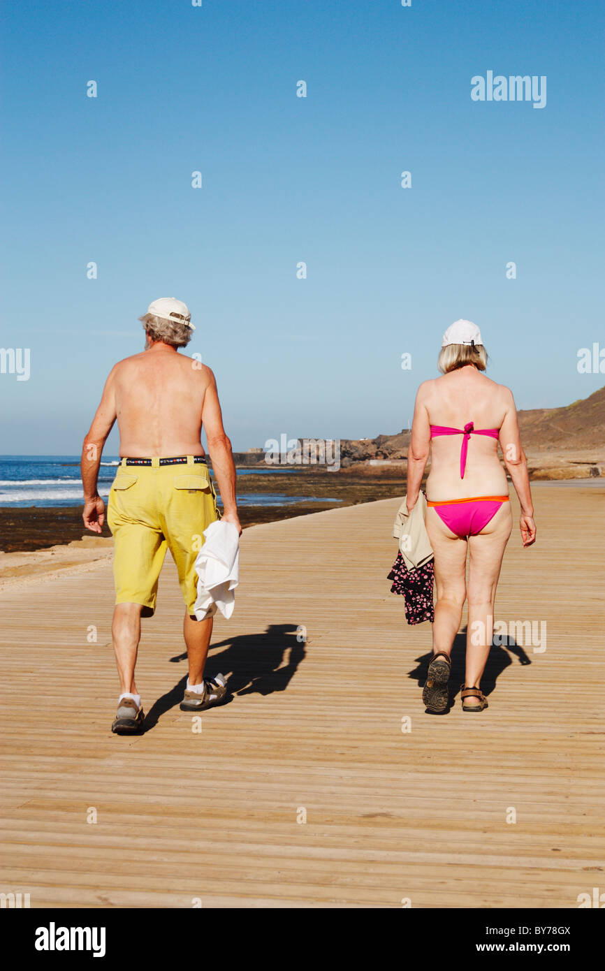 Elderly couple walking on wooden boardwalk near coast in Spain Stock Photo