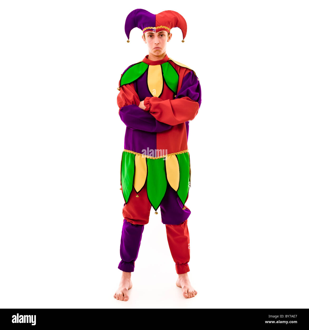 Full length studio shot of a caucasian male Jester, looking miserable with arms folded in a defensive stance.  White background Stock Photo