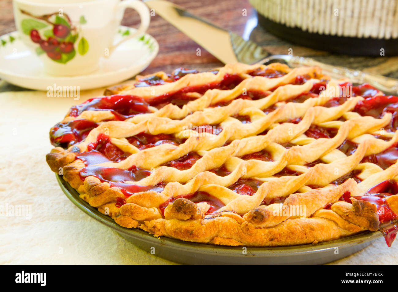 Homemade cherry pie cooling on a table with a tea cup in the background Stock Photo