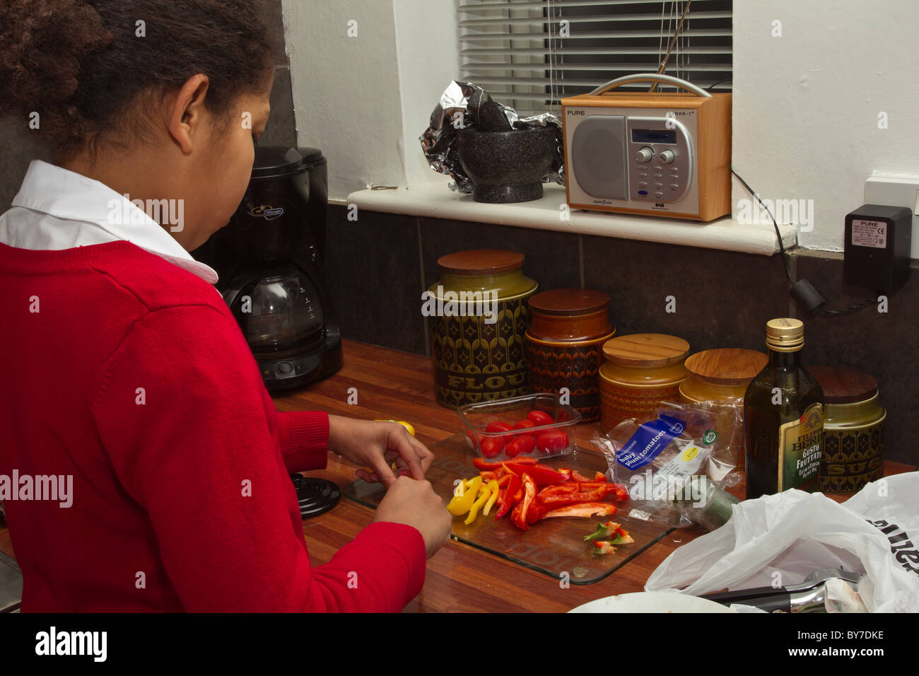 Yong mixed race school girl preparing vegetables in kitchen. Stock Photo