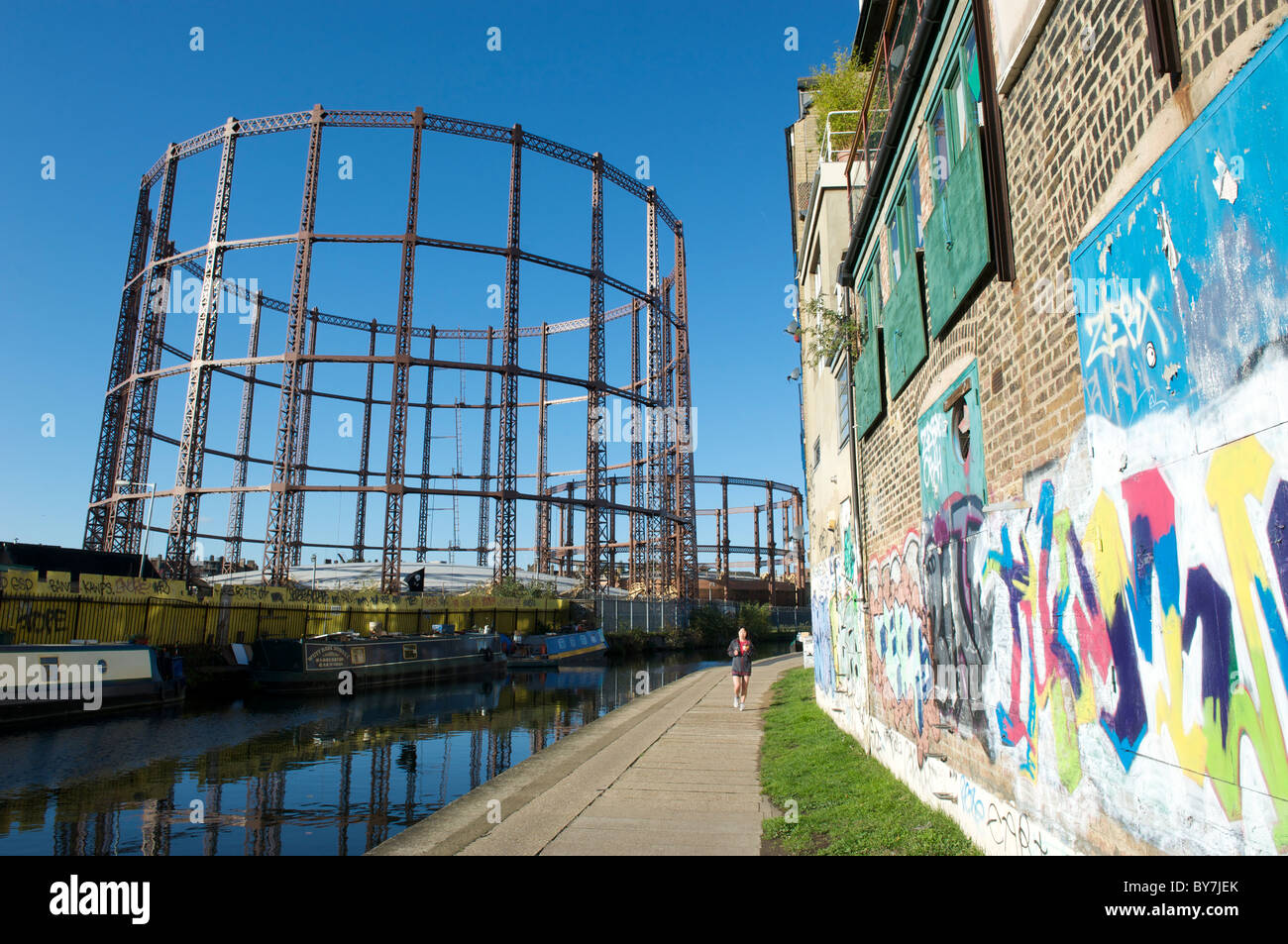 Jogger along Regents canal tow path next to Haggerston gasworks Hackney London by Columbia Road market.  Graffiti on wall. Stock Photo
