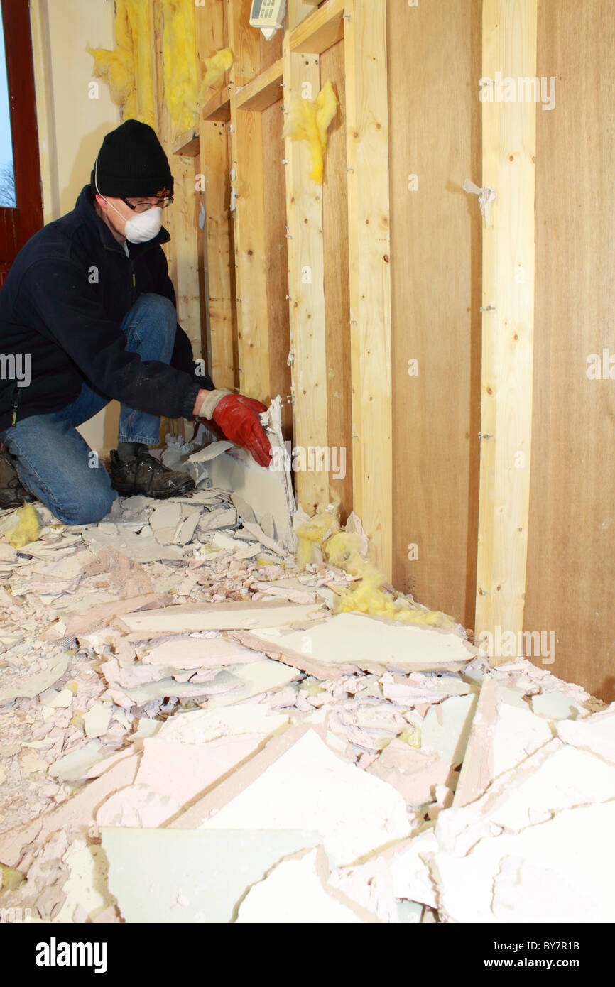 workman removing old plasterboard from a timber-framed wall Stock Photo
