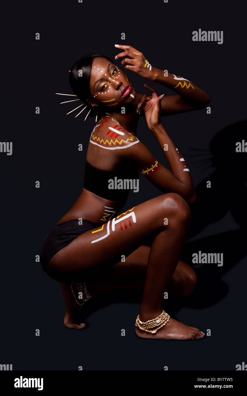exotic African female fashion with tribal yellow red and white makeup cosmetics and sticks in hair, in cultural dance position. Stock Photo