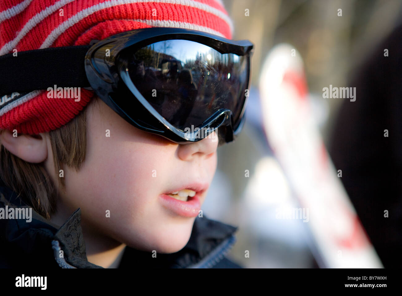 Eight year old boy wearing googles and a red hat, getting ready to ski