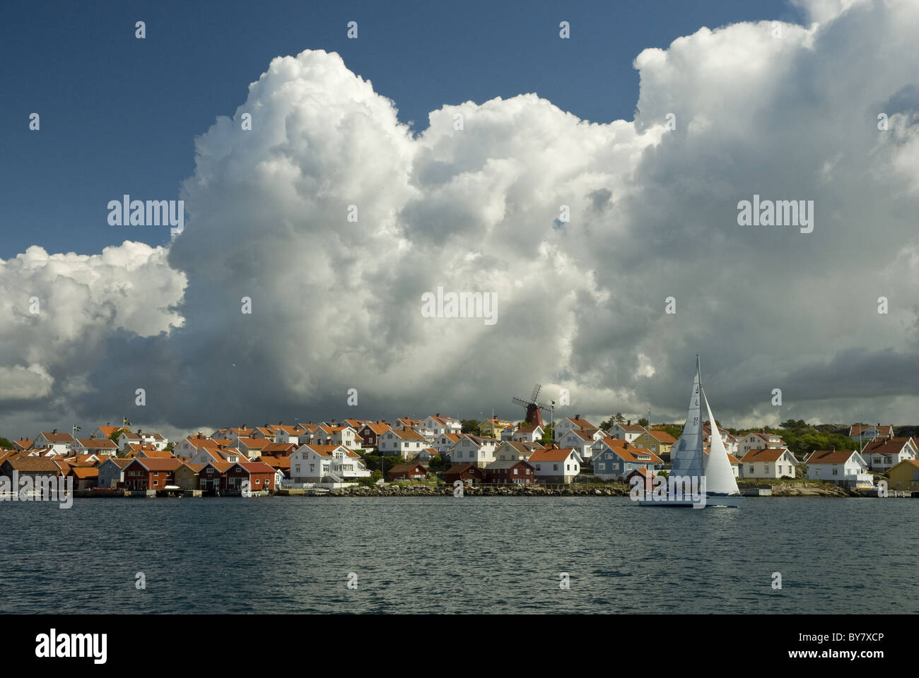 A boat is sailing by one of many small coastal communities on the west coast of Sweden. Thunder clouds are building in the heat. Stock Photo