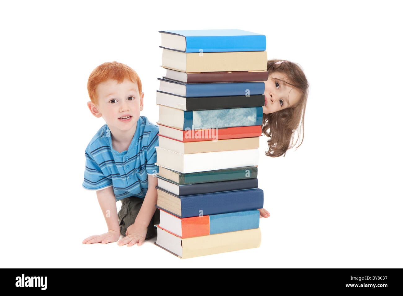 Two kids hiding behind stack of books. Isolated on white. Stock Photo