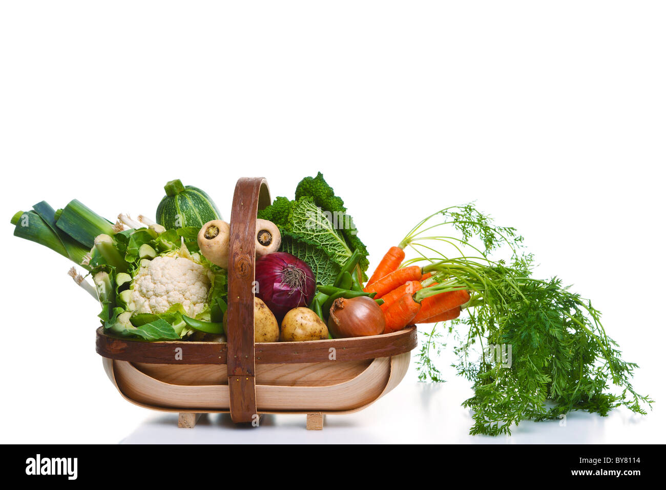 Photo of a wooden trug full of organic vegetables, isolated on a white background. Stock Photo