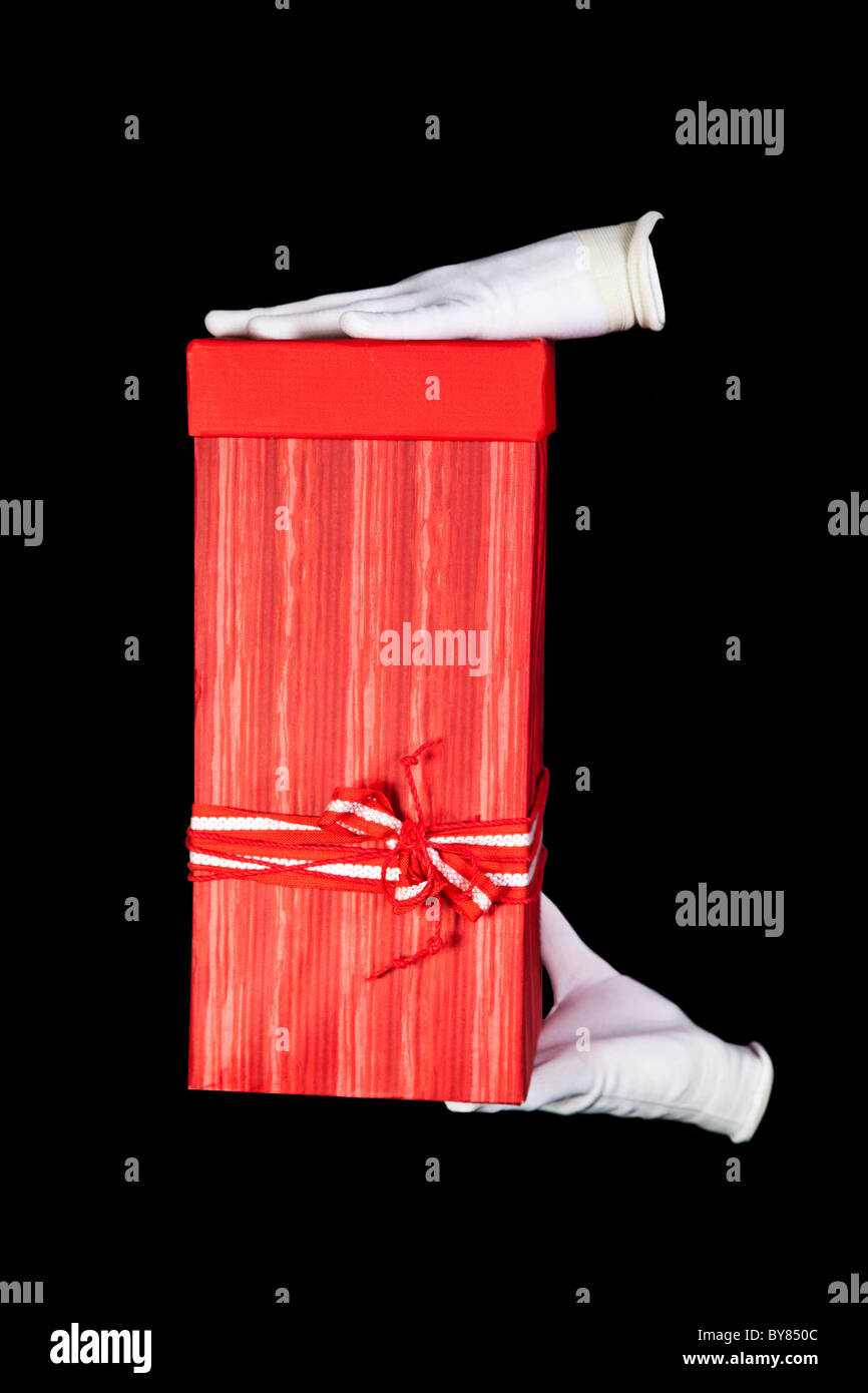 Hands in white gloves with red gift box on black background Stock Photo