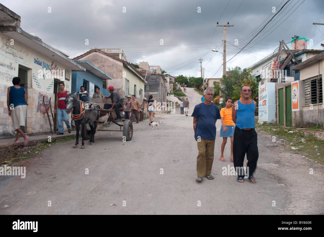 View of a typical small city 's street in Cuba with crowd, houses and horse carriage under grey sky. Stock Photo