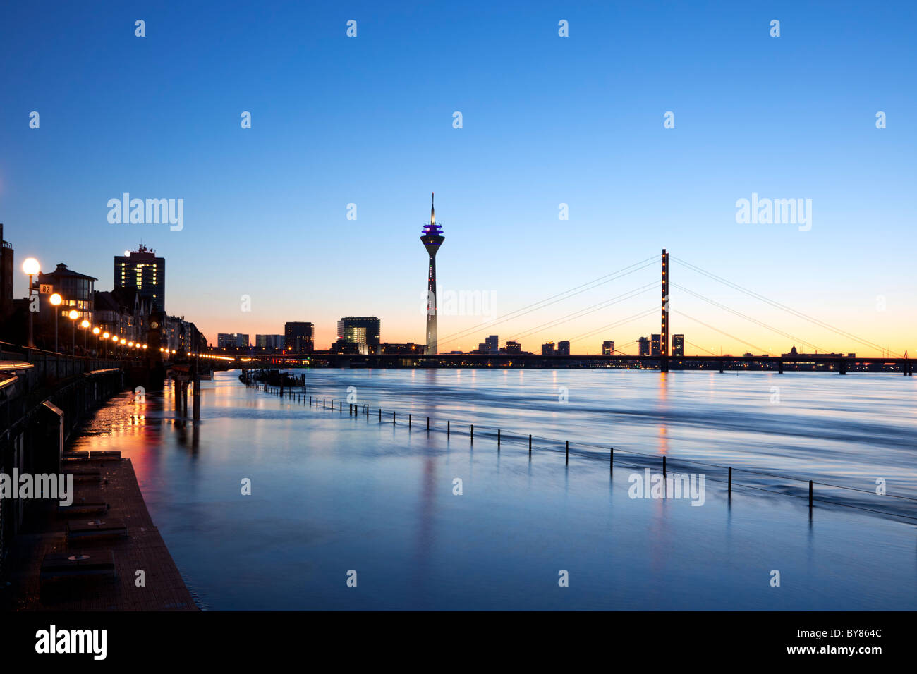 Dusseldorf cityscape with Rhine Promenade, Rhine Tower, Rheinknie Bridge, MediaHarbor, silhouetted against sunset, high tide Stock Photo