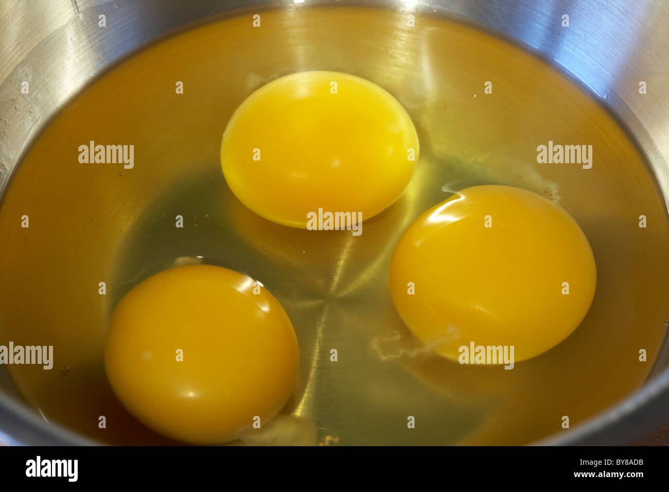 three eggs broken in a metal mixing bowl Stock Photo