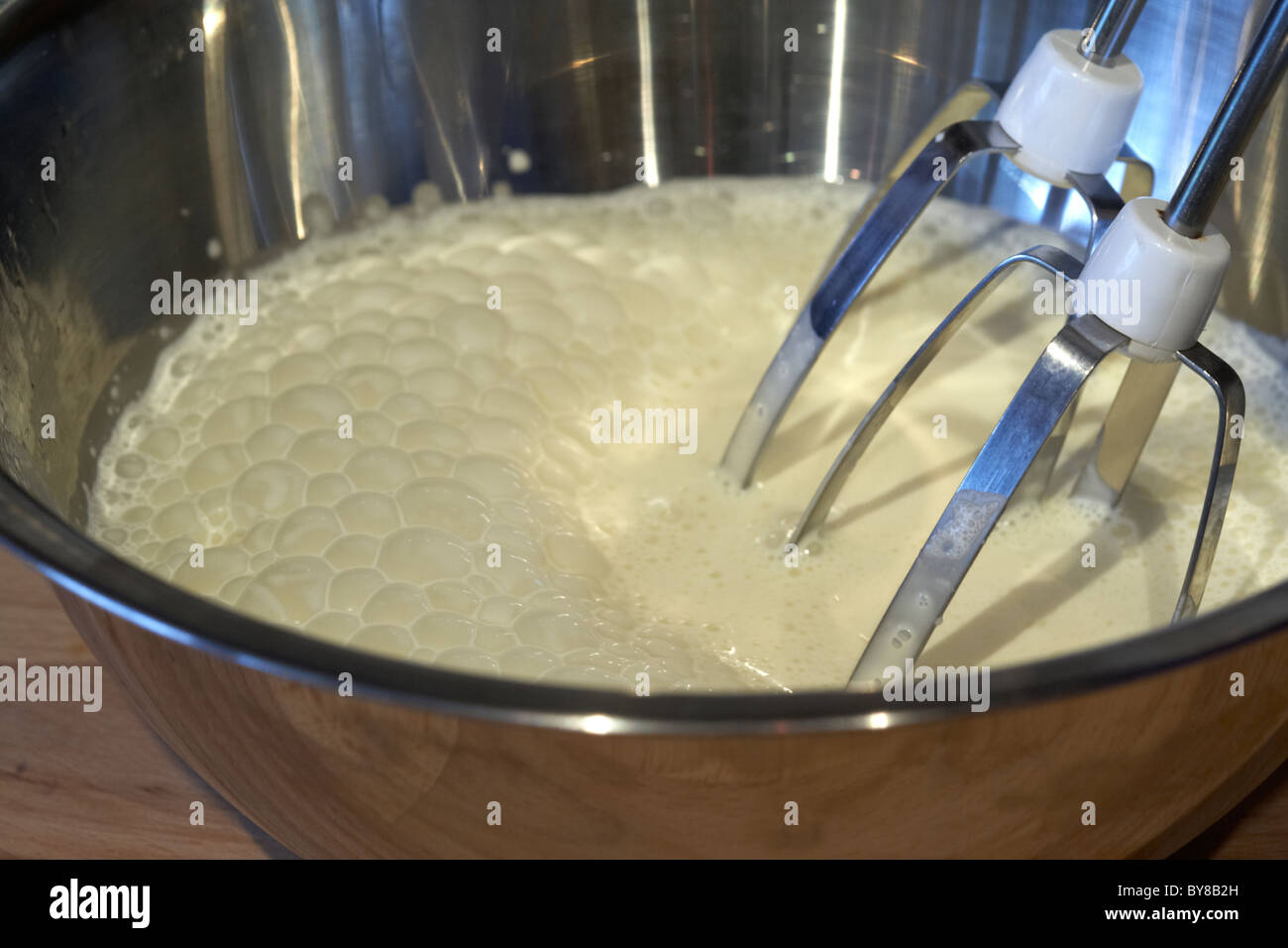 fresh whipping cream in a metal mixing bowl with electric whisk Stock