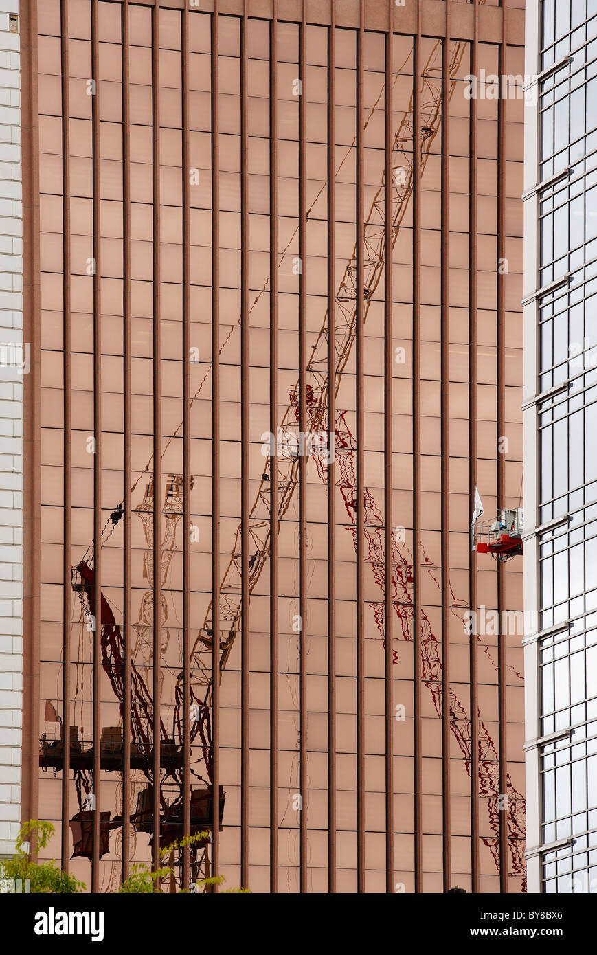 An upright pedestal crane at a construction site, reflected in the mirrored glass of another